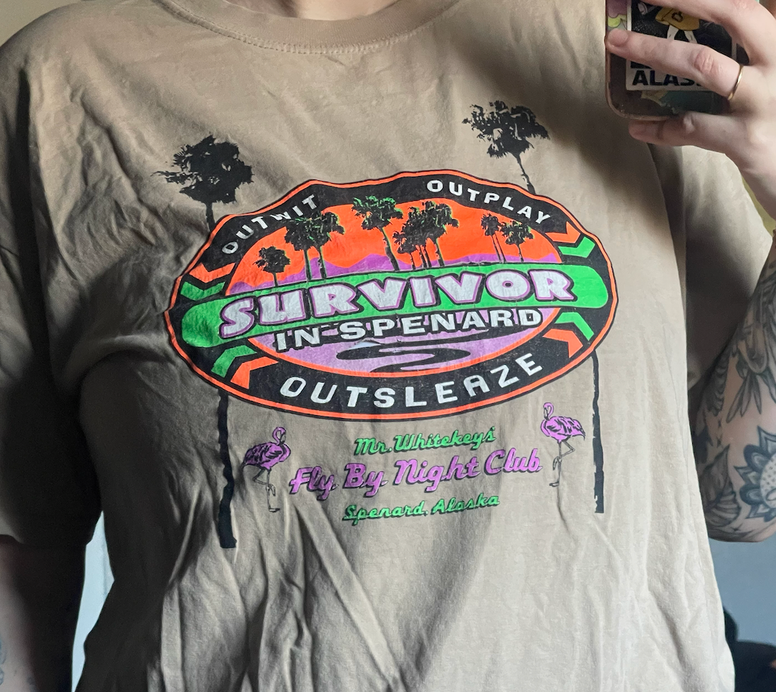 A photo of a tan shirt with text that reads "Survivor in Spenard: Outwit, Outplay, Outsleaze. Mr Whitekeys' Fly By Night Club, Spenard Alaska.